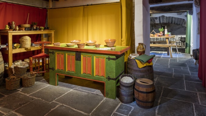 The trading area inside Tudor Merchant's House, Pembrokeshire, which has a low, wooden-beamed ceiling, flagstone floor, barrels and a green sideboard with terracotta bowls on it.